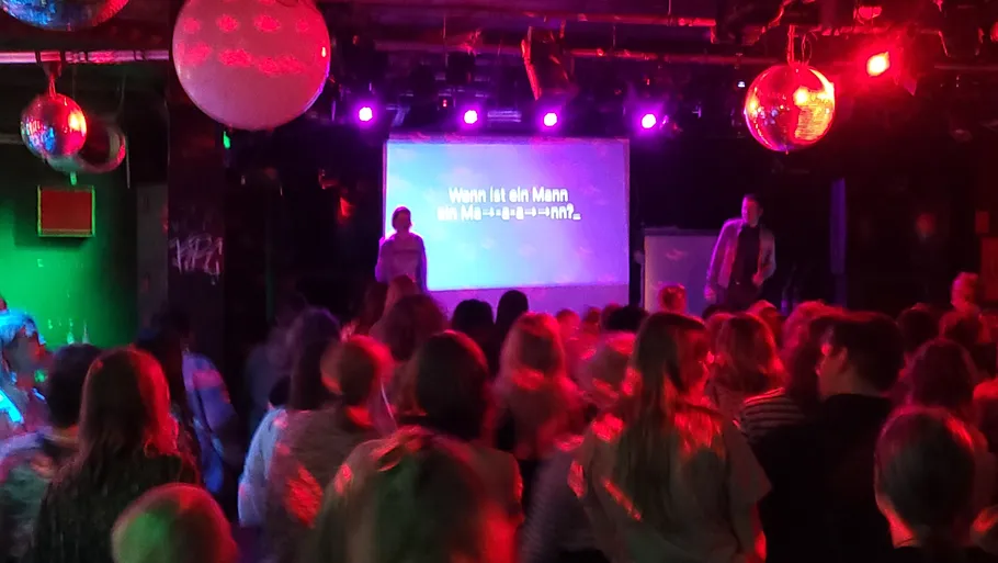 Crowd watching karaoke performance in colorful club.