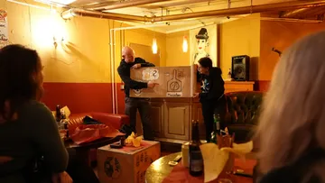 Zwei Personen präsentieren Plakat in gemütlicher Bar.