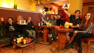 People in a bar holding letter cards.