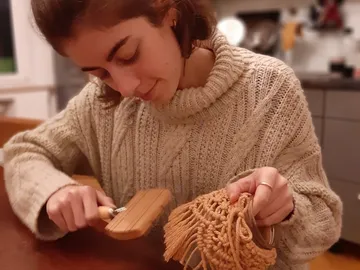 A young woman uses a tool to work on a handmade object.