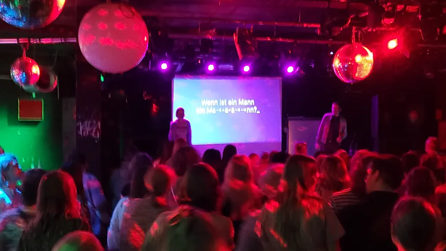 Crowded room with karaoke on stage.