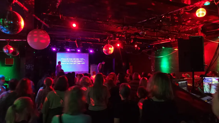 Crowd watching karaoke in dark nightclub.