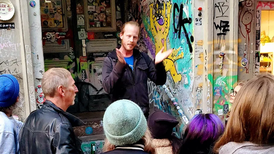 Man speaking to group in graffiti-covered alley.