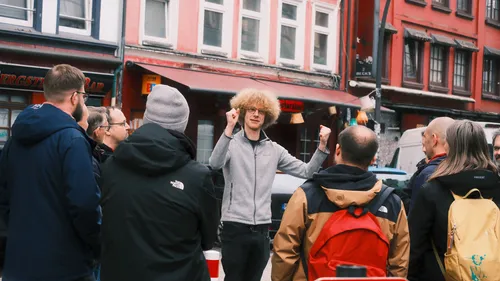 Man gestures energetically to group on city street.