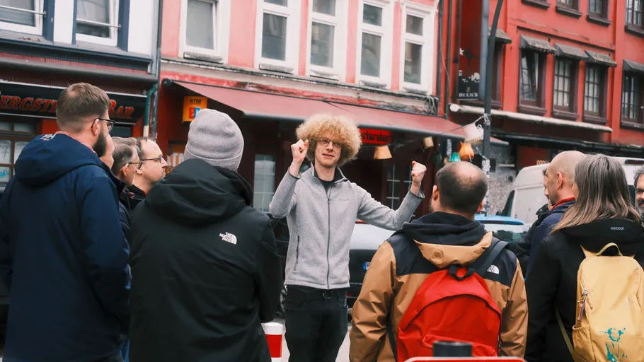 Man gestures energetically to group on city street.