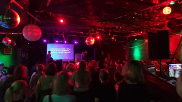 Menschenmenge schaut Karaoke in dunklem Club.