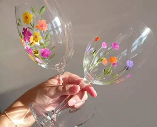 Hände halten blumenbemalte Weingläser.