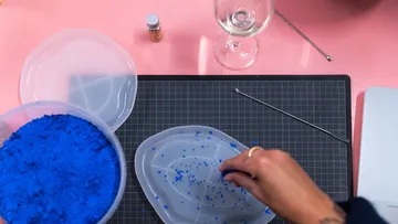 Person crafting with blue material on pink surface.