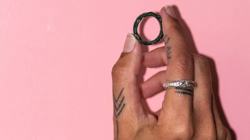 Hand hält Ring vor rosa Hintergrund.