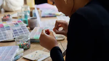 Frau fertigt Schmuck an einem Basteltisch.