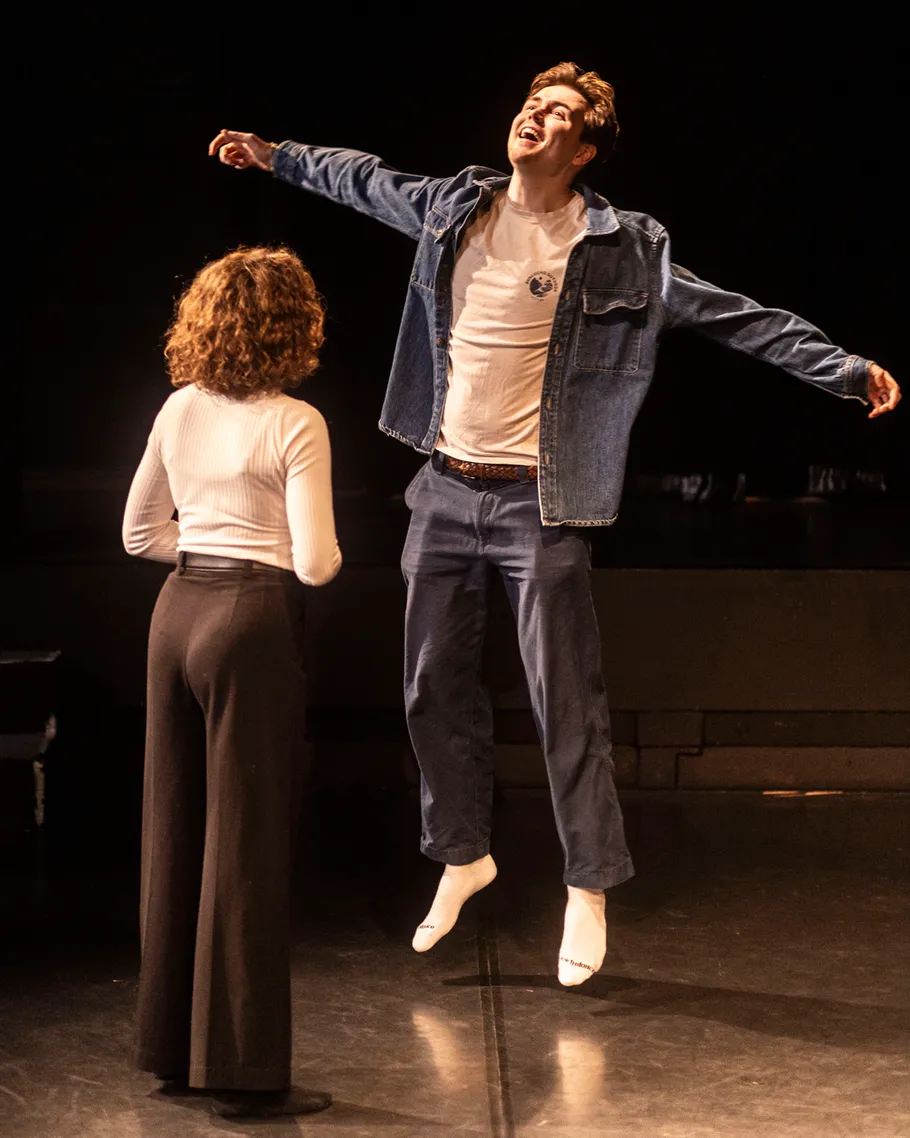 Man jumping joyfully on stage with woman nearby.