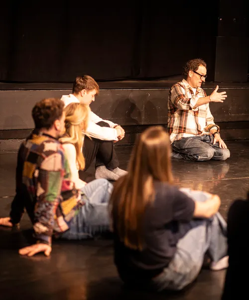 Group sitting on stage, person gestures mid-speech.