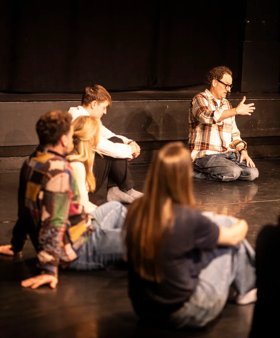 Group sitting on stage, person gestures mid-speech.
