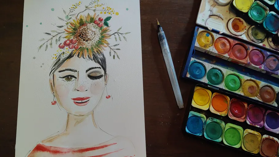 Watercolor portrait with floral headpiece beside paints.