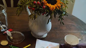 Sonnenblumen in Vase auf Holztisch mit Malutensilien.