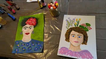 Two painted portraits on a covered table.