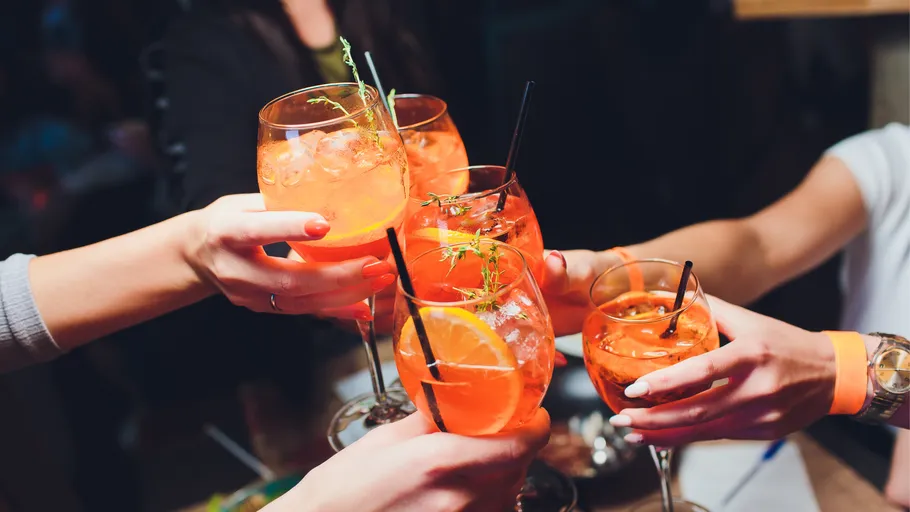 Hands holding orange cocktails in celebration.