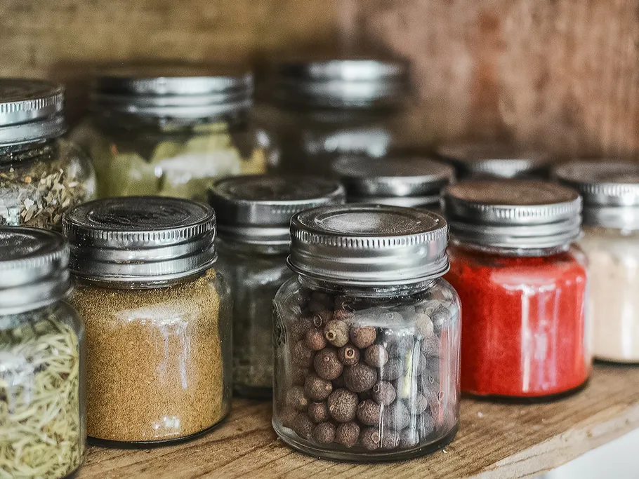 Jars with spices are placed on a wooden shelf.