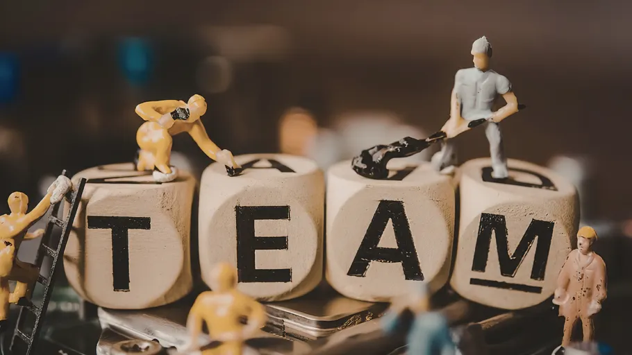Miniaturfiguren arbeiten an TEAM-Buchstabenblöcken.