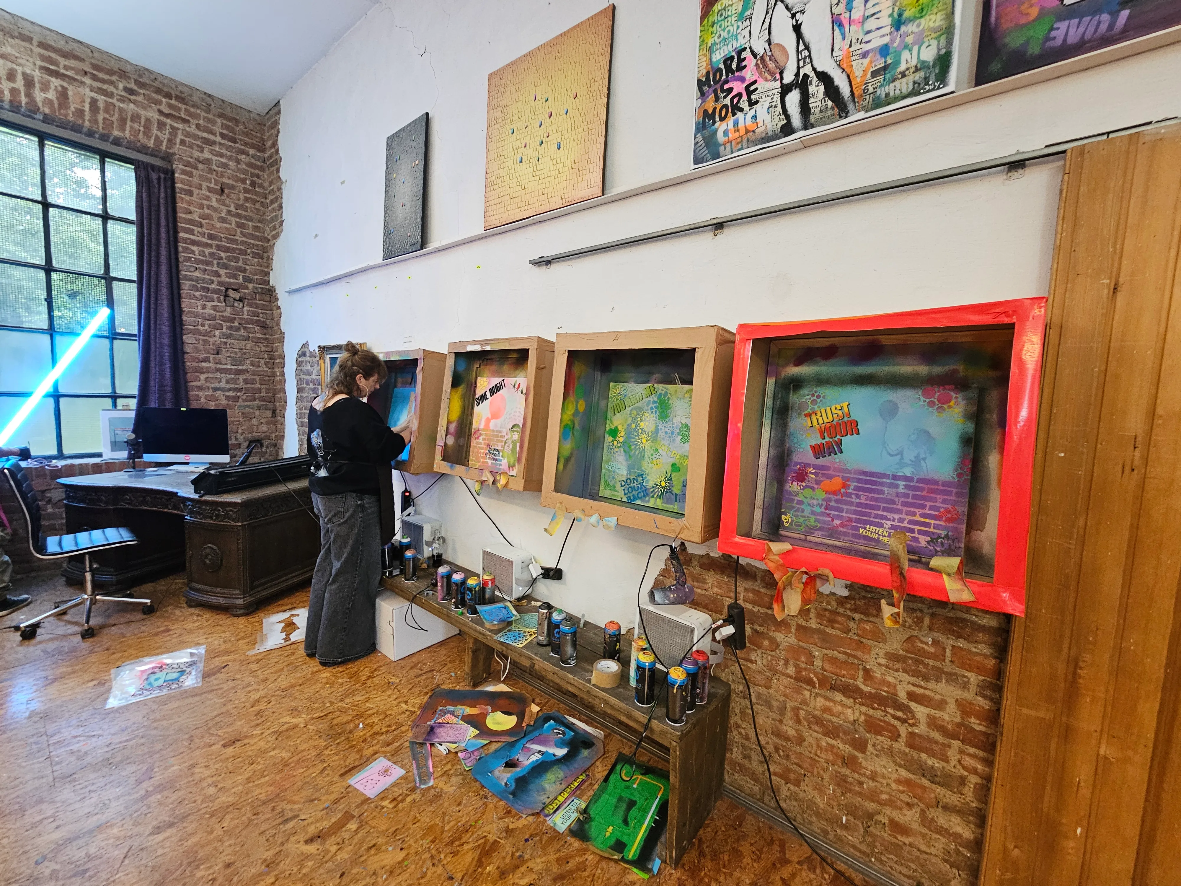 Artist painting in studio with canvases on wall.
