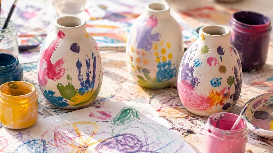 Three painted vases on a messy art table.