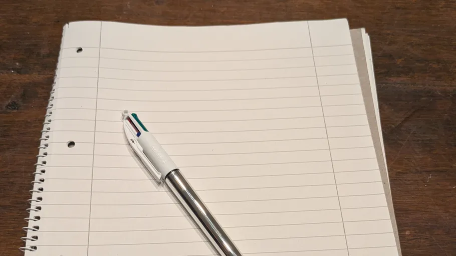 Pen on a lined notebook, wooden table.