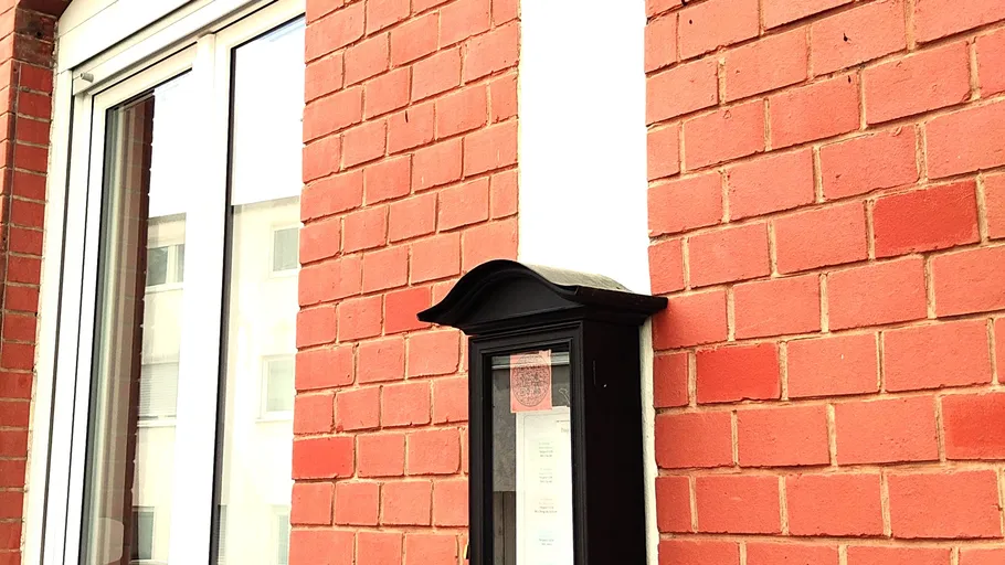 Black mailbox on brick wall near window.