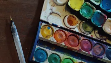 Paintbrush and watercolor palette on wooden table.