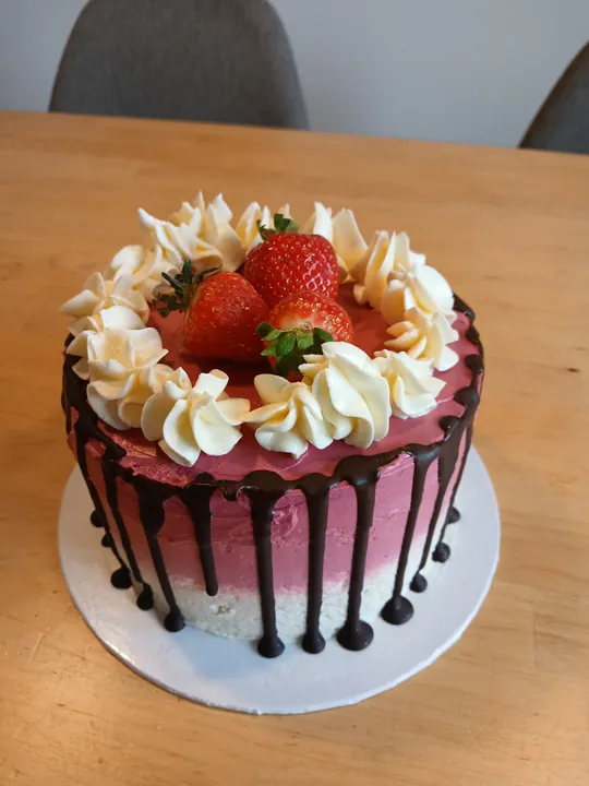 Strawberry cake with chocolate drips on table.