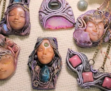 Handmade face pendants with gemstones on fabric.