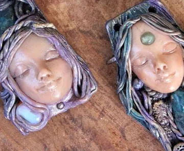Two decorative clay faces with braided hair.