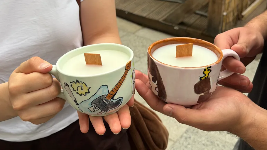 Two hands holding decorated mugs with drinks.