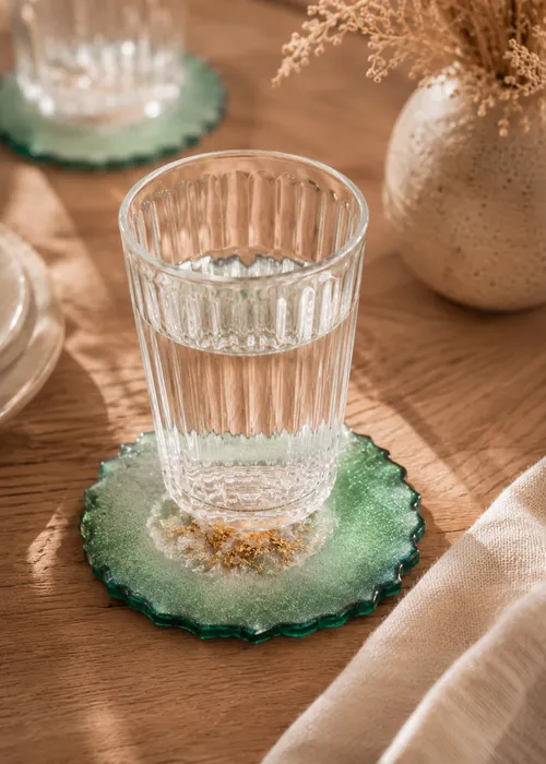 Glass of water on green coaster, wooden table.