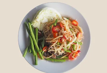 Papaya salad with vegetables on white plate.