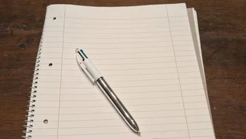 Pen on spiral notebook, wooden desk.