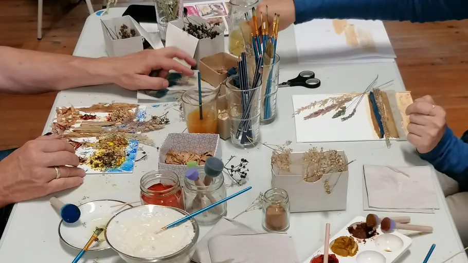 Hände basteln mit getrockneten Pflanzen am Tisch.