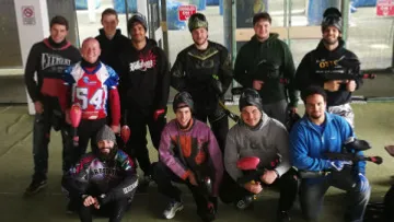 Group posing with paintball gear indoors.