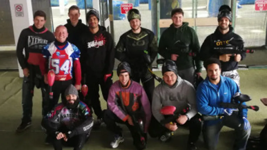 Group posing with paintball gear indoors.