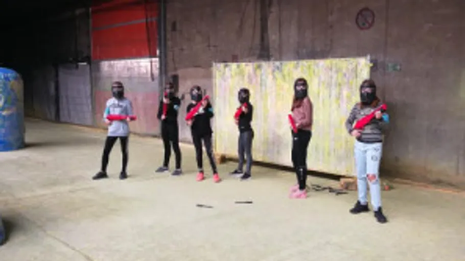 Personen in Schutzkleidung mit Paintball-Waffen drinnen.