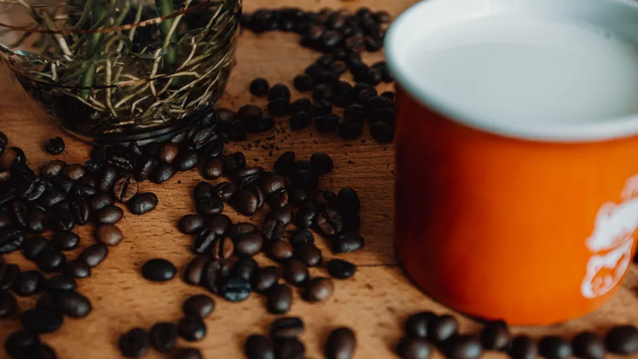 Coffee beans scattered near orange mug.