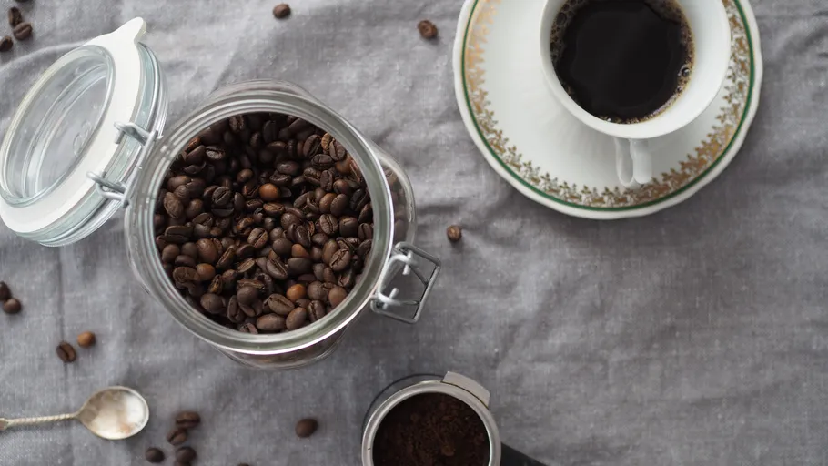 Coffee beans in jar near coffee cup.