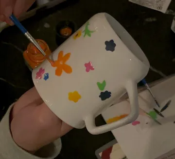 Person malt bunte Blumen auf Tasse.