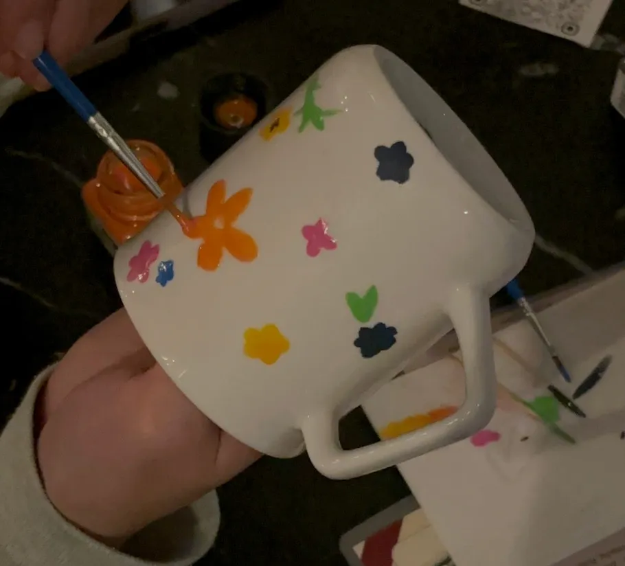 Person malt bunte Blumen auf Tasse.