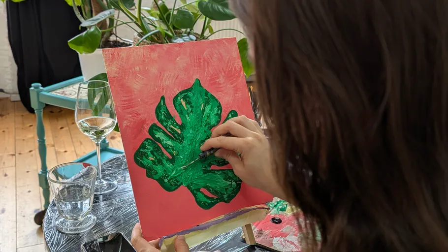 Person painting green leaf on canvas indoors.