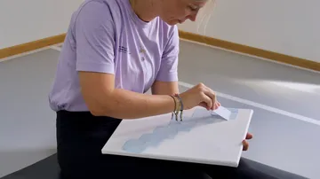 Person peeling stickers on a canvas indoors.