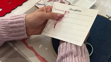 Hand näht auf Übungsblatt, Tischhintergrund.