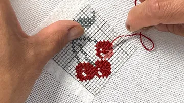 Hände sticken Kirschen auf weißem Stoff.