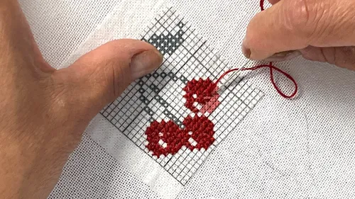Hände sticken Kirschen auf weißem Stoff.