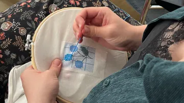 Person embroidering pattern in wooden hoop.