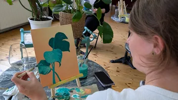 Person malt Blätter an einem Tisch drinnen.